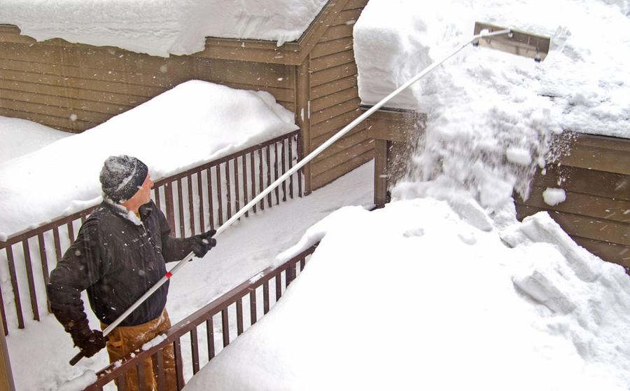 man using roof rake to remove roof snow on a garage